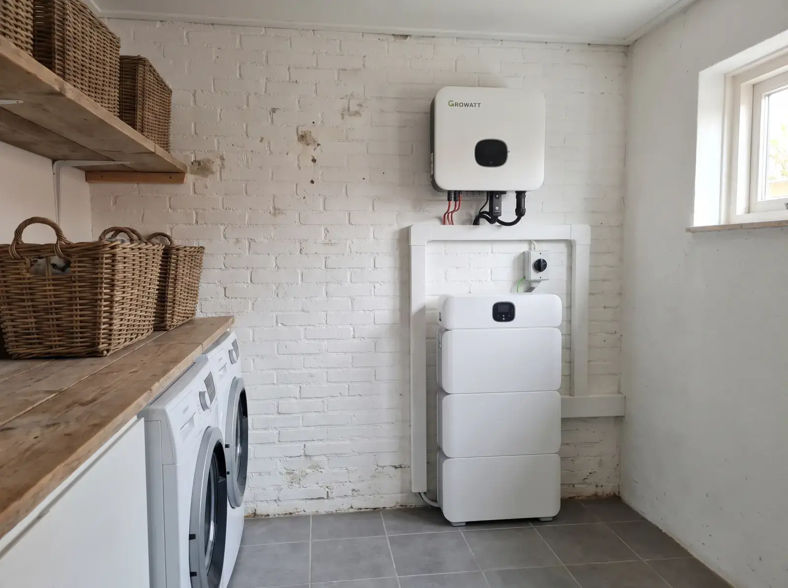Witte Growatt-thuisbatterij naast de omvormer aan de muur van een bijkeuken